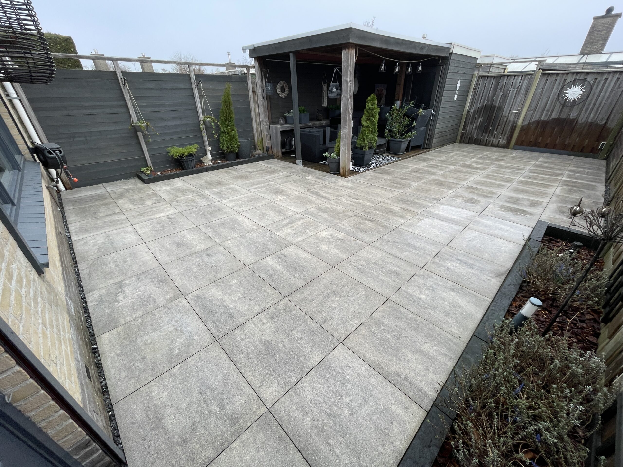 Een foto van een schoongemaakt terras, waarbij de natuurlijke kleur van de tegels weer zichtbaar wordt onder de groene aanslag.